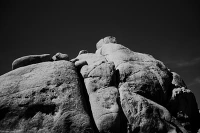Black and white view of a stacked granite outcrop lit by low sun, rising against an almost black sky.