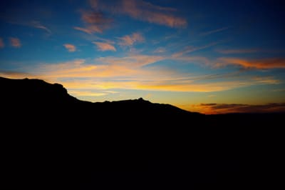Dark ridgeline silhouetted against a blue and gold sunset sky streaked with wispy orange clouds.